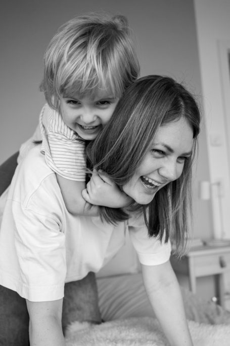 Eine lachende Frau mit einem Kind, das ihr auf dem Rücken sitzt. Beide strahlen Freude aus.