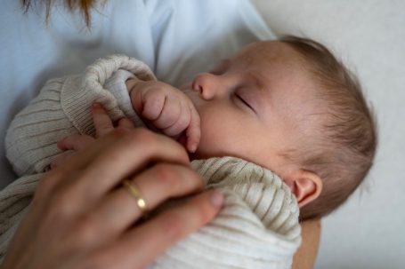 Ein schlafendes Baby mit einer Hand in den Mund, sanft gehalten von einer Person.