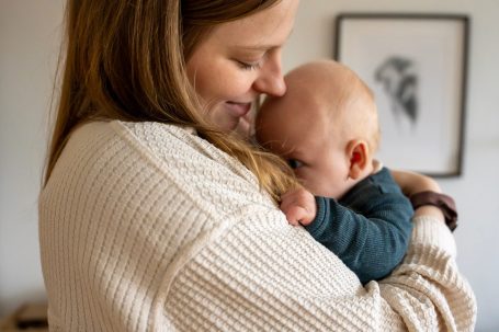 Frau umarmt ein Baby, beide wirken liebevoll und geborgen in einem hellen Raum.