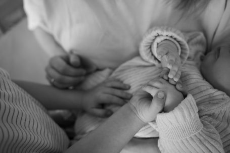 Hände eines Kleinkinds und einer erwachsenen Person, die ein neugeborenes Baby halten.