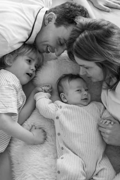 Eine Familie liegt zusammen auf dem Boden, das Baby lächelt, während die Eltern und Geschwister spielen.