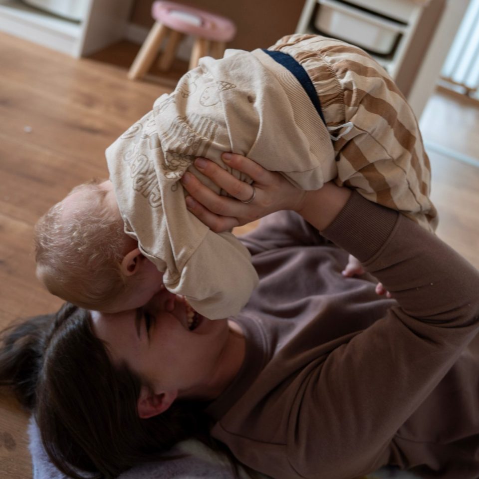 Familienfotografie Eine Mutter hebt ihr lächelndes Kind spielerisch über sich.