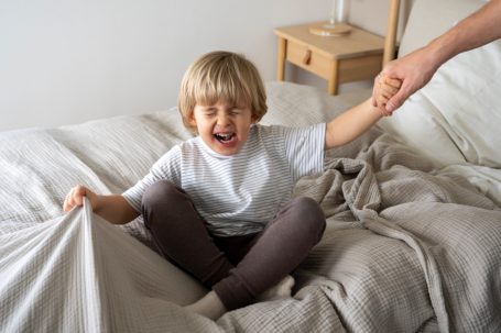 Ein Kind sitzt auf einem Bett, lacht und greift nach der Hand eines Erwachsenen.