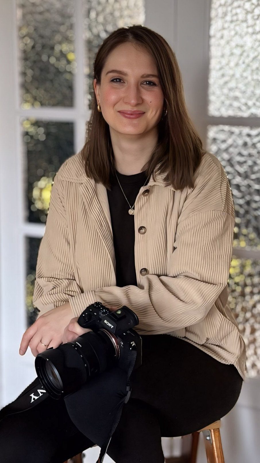 Familienfotografin in Buchholz in der Nordheide Junge Frau mit Kamera in einer hellen Umgebung, lächelt entspannt in die Kamera.